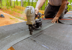 Roofer using a nail gun to install new shingles on a residential roof in Norman, highlighting expert roofing services by Warrior Roofing Solutions.