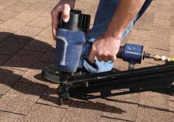 Close-up of a roofer using a nail gun to install shingles on a residential roof in Yukon, showcasing expert roofing services by Warrior Roofing Solutions.