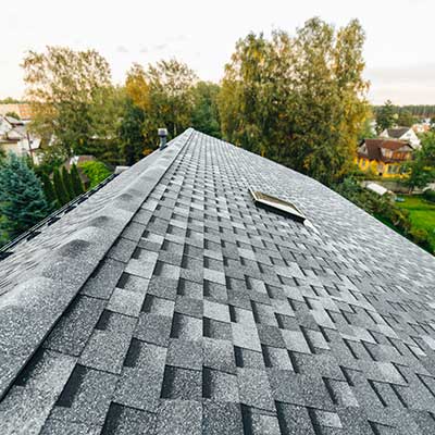 Side and close up view of a residential roof with gray shingles and tress in the background