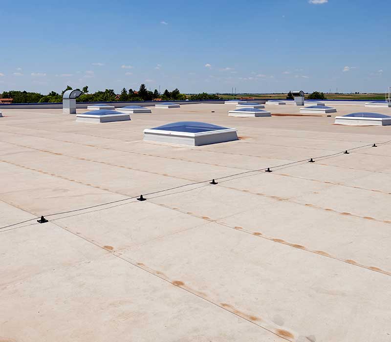 Overview of a large flat commercial roof with the top of skylights dotted all across it