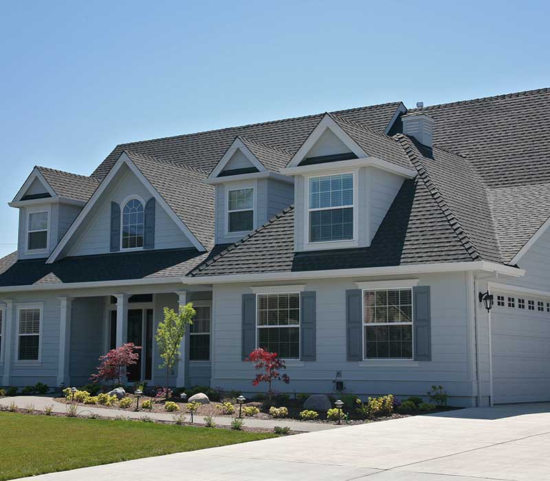 Front view of a large, mid-class and light-gray home with gray shingles on its roof