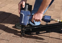Close-up of a roofer using a nail gun to install shingles on a residential roof in Yukon, showcasing expert roofing services by Warrior Roofing Solutions.